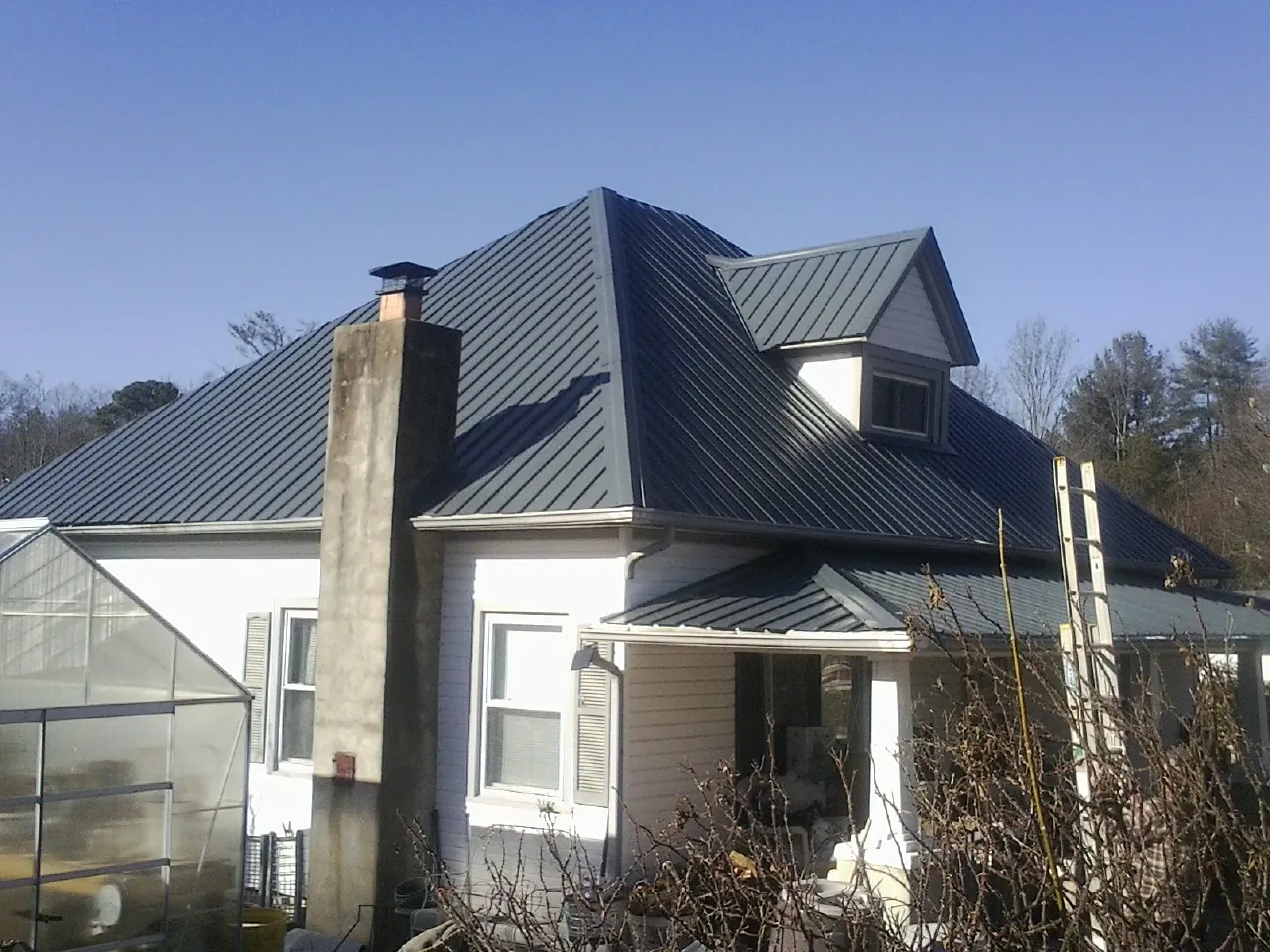 Dark blue standing seam metal roof on a white farmhouse with dormer — Slate & Tile Roof Repair by Roofing Brothers in Harlowton