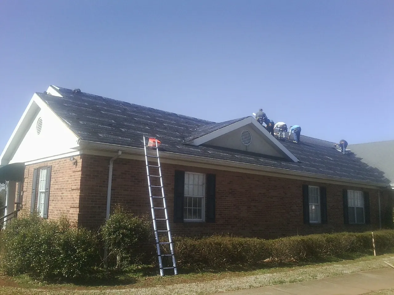 Crew tearing shingles off a brick ranch roof with a ladder set — Metal Roof Repair work by our crew in Harlowton