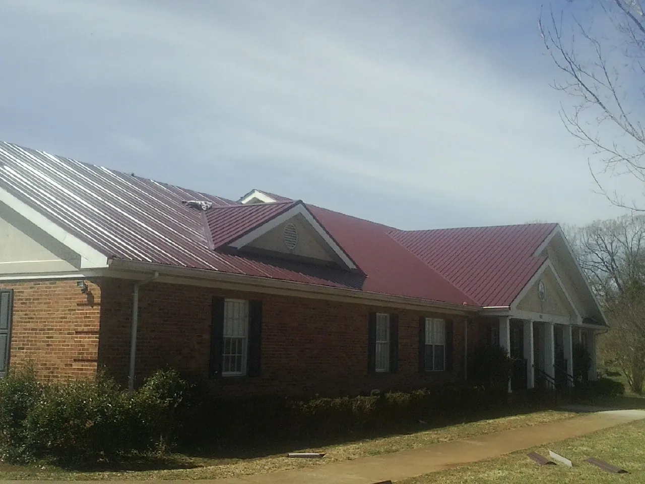 Red metal roof with gabled entries on a long brick building, from a Hail Damage Roof Repair job in Harlowton