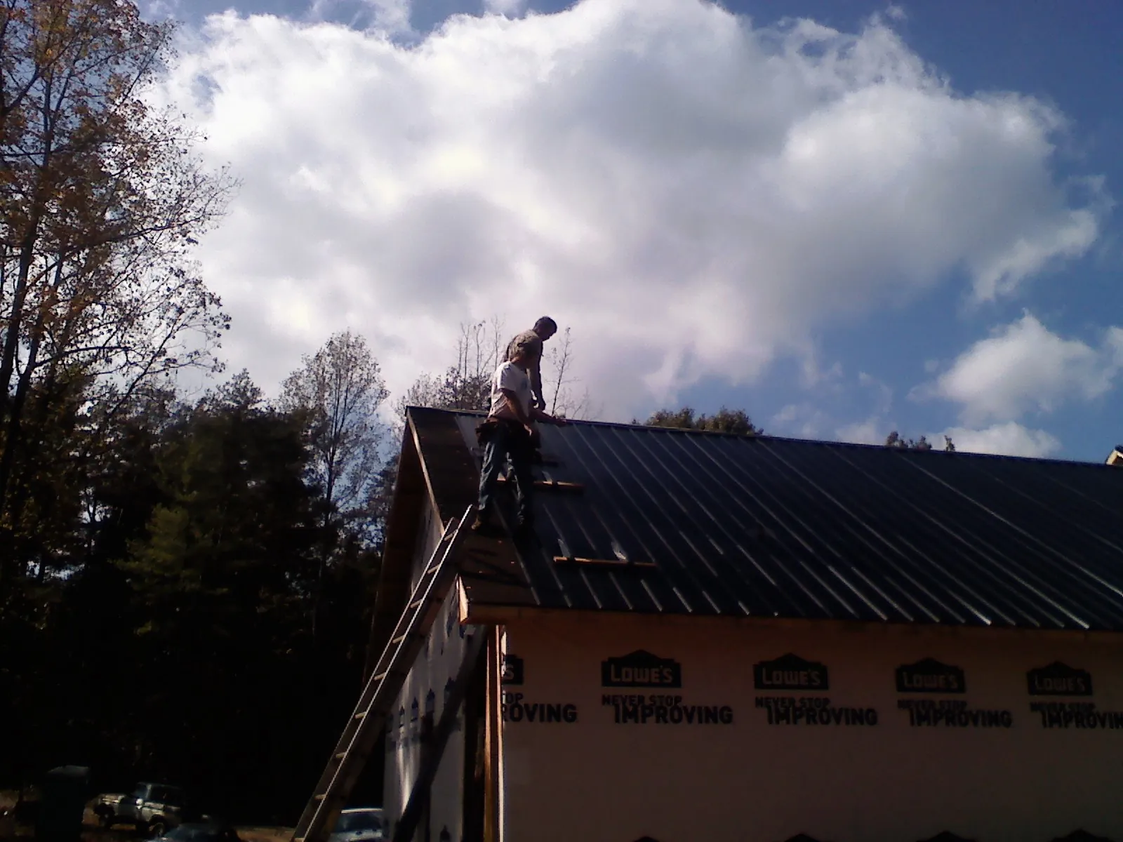 Roofer fastening dark metal panels high against a cloudy sky, from a Roof Inspection job in Harlowton