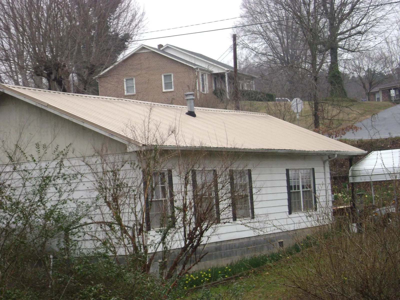 Tan metal roof on a white sided house set into a hillside — Commercial Roofing by Roofing Brothers in Harlowton